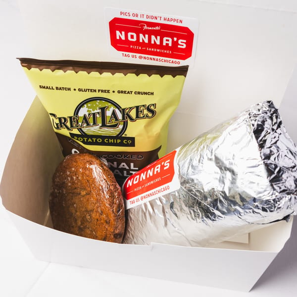 A Nonna's lunchbox with a foil-wrapped sandwich, Great Lakes potato chips, and a wrapped cookie.