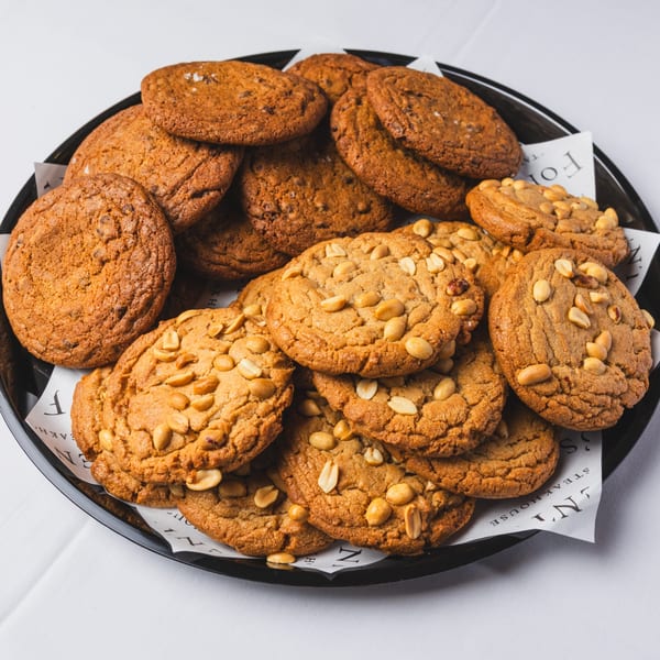 A black platter filled with various cookies, including chocolate chip and peanut butter, on white paper.