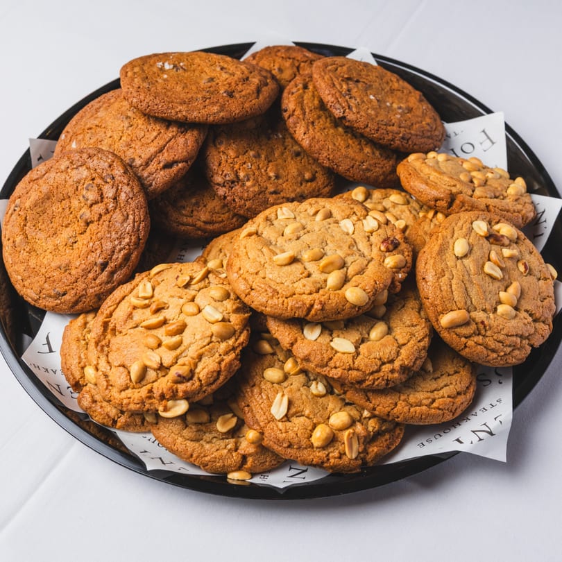 A black platter filled with various cookies, including chocolate chip and peanut butter, on white paper.