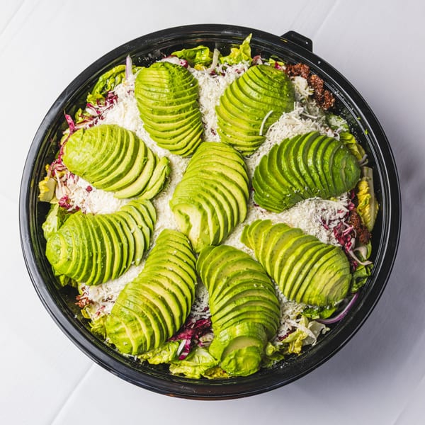 Overhead view of a salad in a black bowl, topped with sliced avocado and shredded cheese.